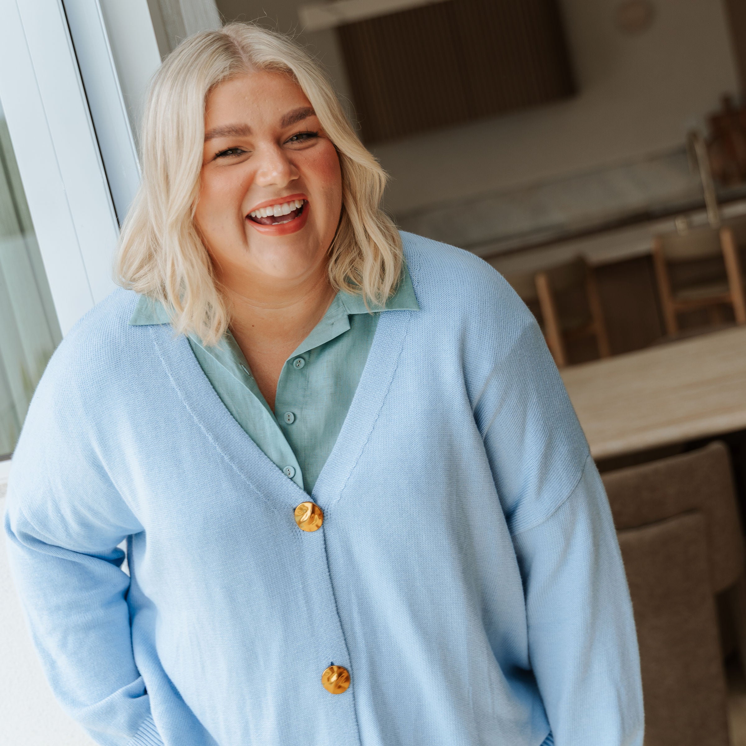 Woman wearing a light blue cardigan with yellow buttons indoors.