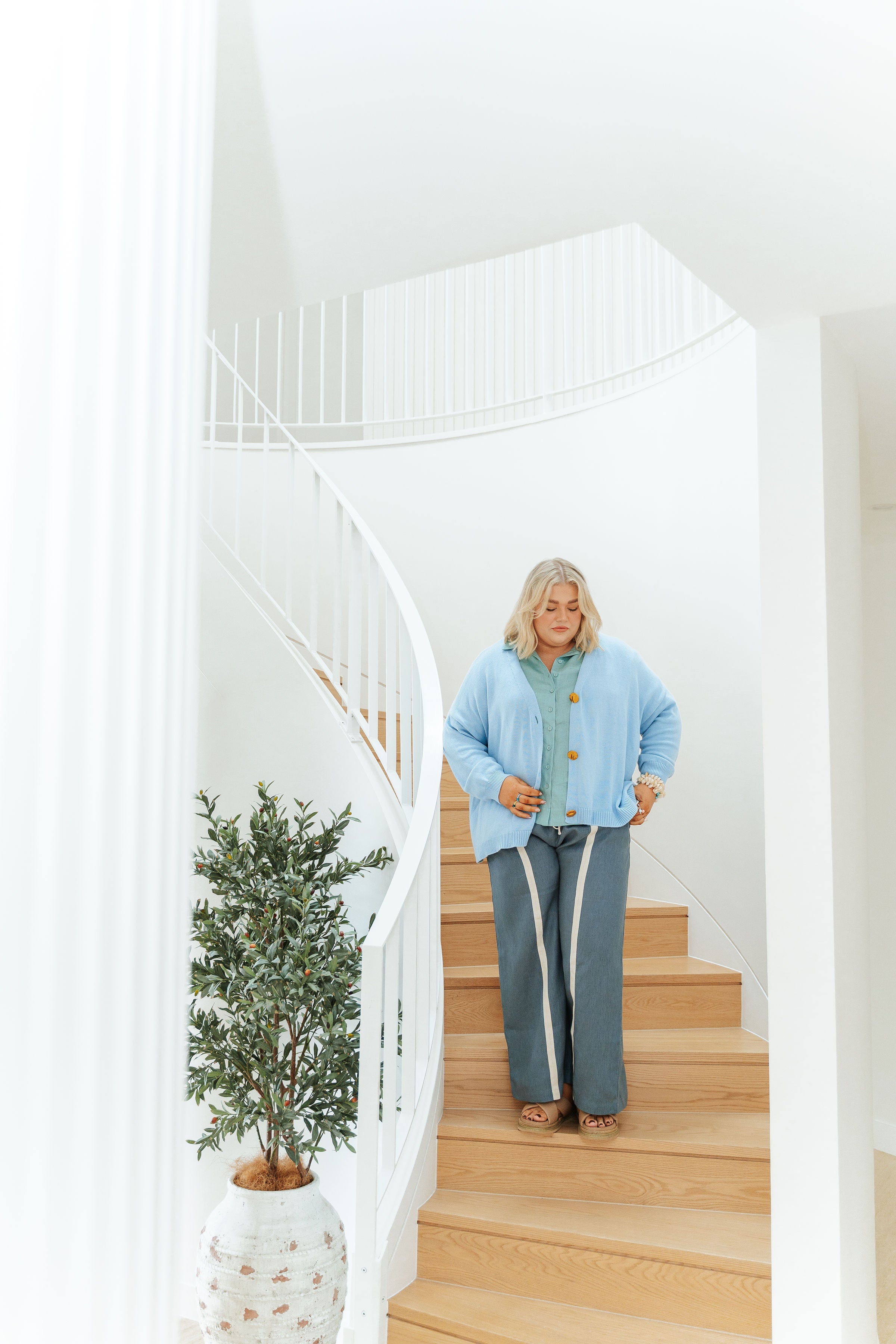 Woman standing on a staircase holding a walking stick in a bright, modern home.