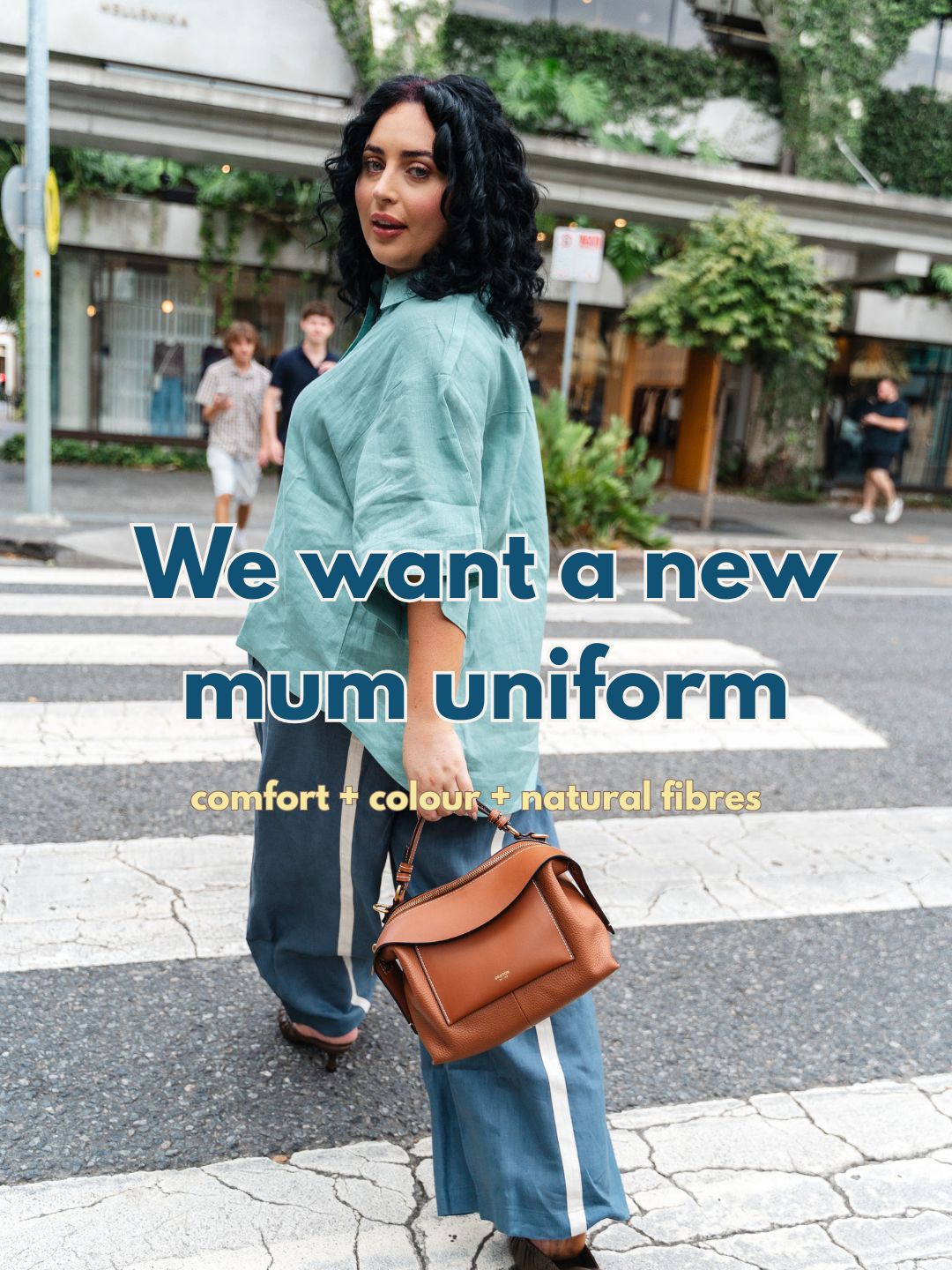 Woman walking on a city street with text 'We want a new mum uniform' and 'comfort + colour + natural fibres'.