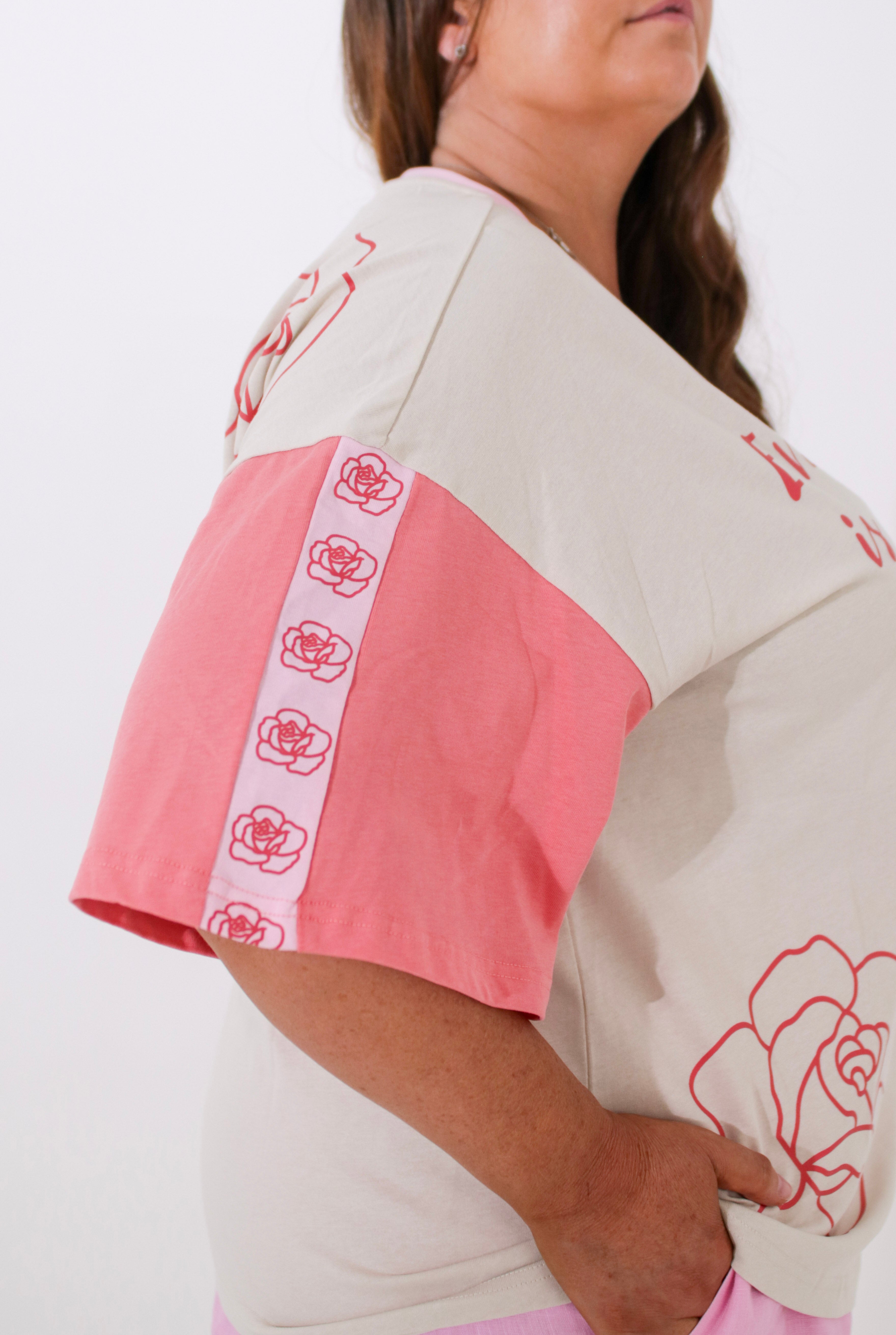 Woman wearing a white blouse with pink accents and floral patterns on a plain background